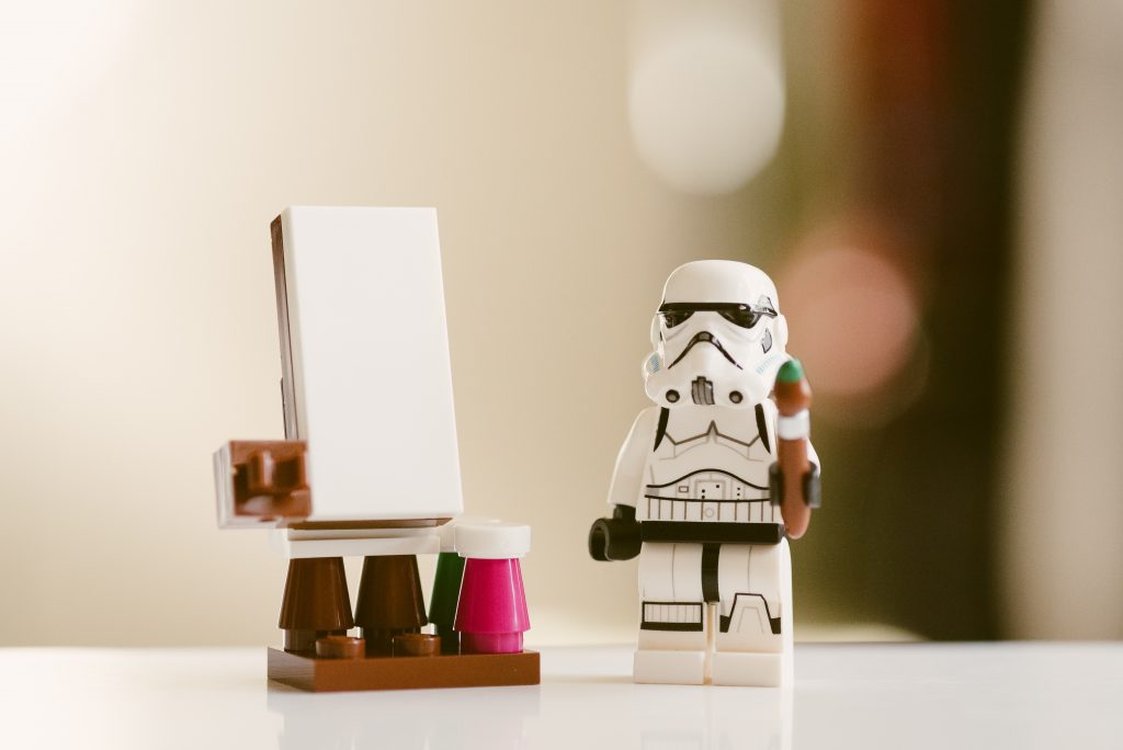 Lego storm trooper holding a paintbrush next to an easel. 