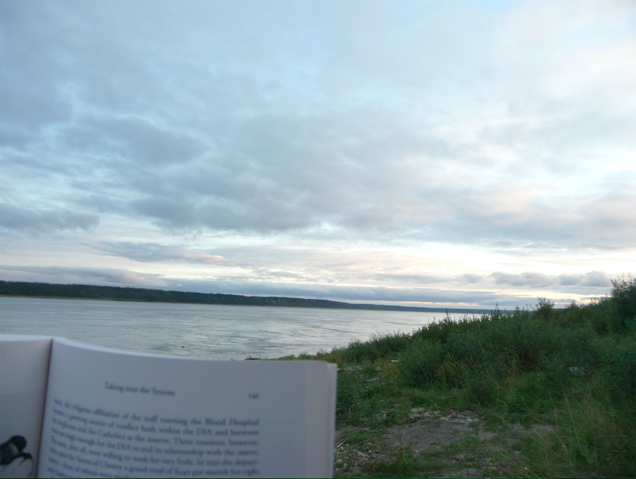 Reading for PhD Comprehensive Exams at Diighe’tr’aajil, Northwest Territories, with the Nagwichoonjik in the background. Photo Credit: Crystal Fraser.