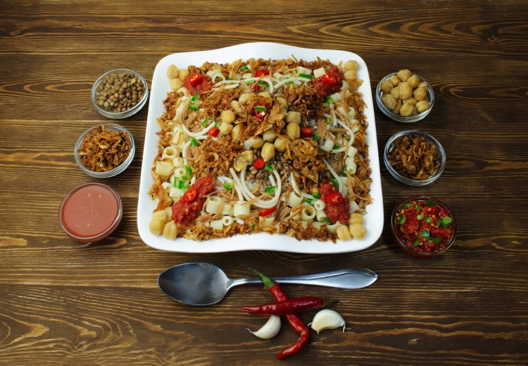 Kushari is made of rice, macaroni, and lentils mixed together, topped with tomato-vinegar sauce, garnished with chickpeas and crispy fried onions and sprinkled with garlic juice and hot sauce