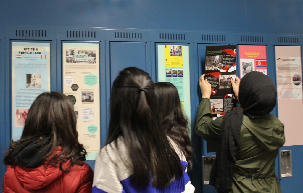 Four students hanging items on blue lockers.