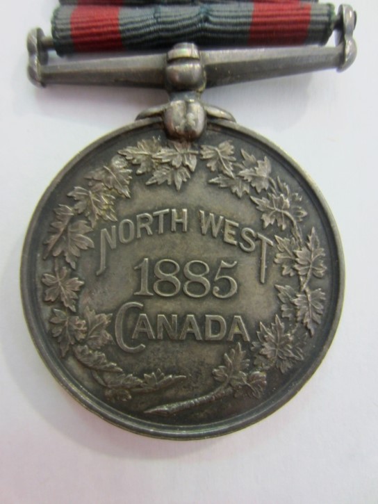 An image of a medal inscribed with the words “North West 1885 Canada.” The edges of the medal are inscribed with a depiction of a maple leaf wreath.