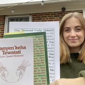 Photo of a blonde woman in a green sweater holding three books. The book at the front of the stack is titled "Kanyen'keha Tewatati (Let's Speak Mohawk)."