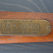 Close-up photograph of a brown piece of wood. There is a brass plate affixed with these words embossed on it: “From the teak of H.M.S. Ganges, the last sailing ship to serve as a seagoing flagship.”