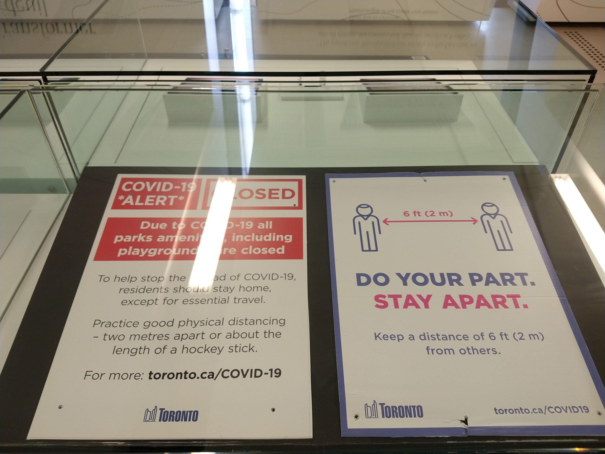 Photo of two signs in a glass display case. The signs remind the reader to practice social distancing.