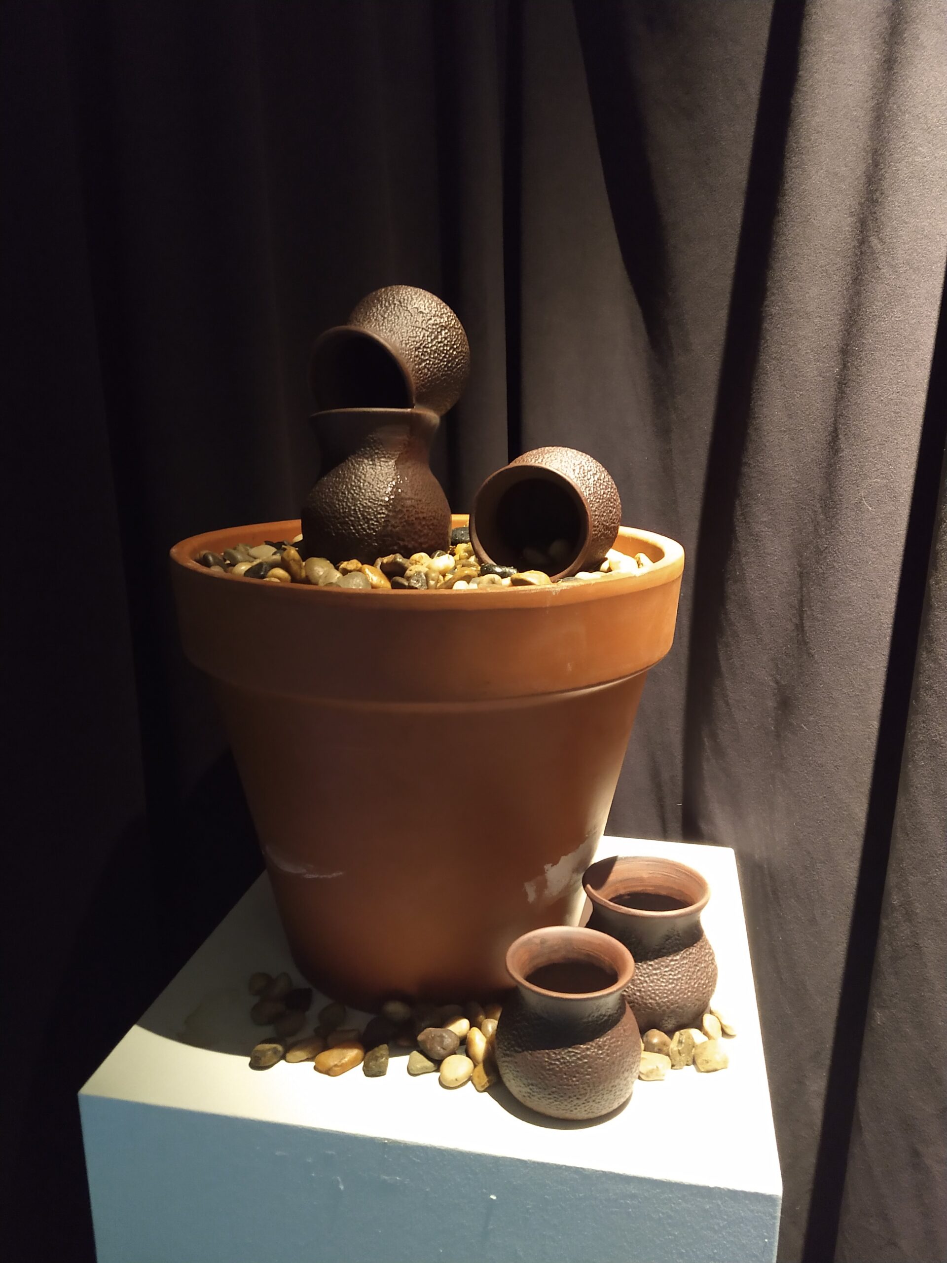 A large pot full of pebbles. There are four smaller pottery cups, two on top of the pot of pebbles and two next to it.