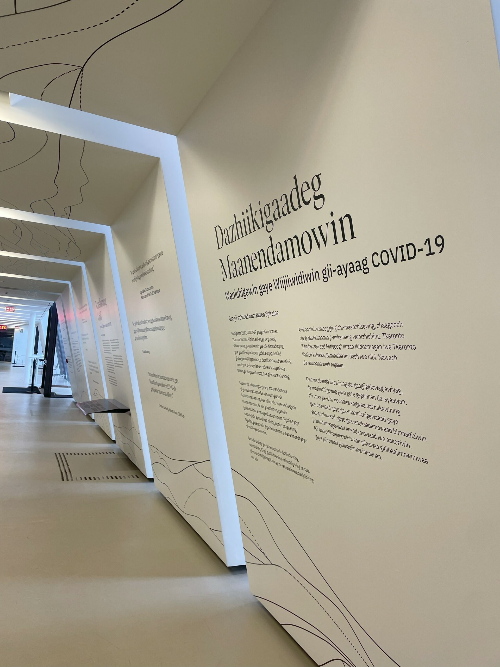 Black text on the white walls of a hallway. There are windows and skylights placed evenly along the hall.