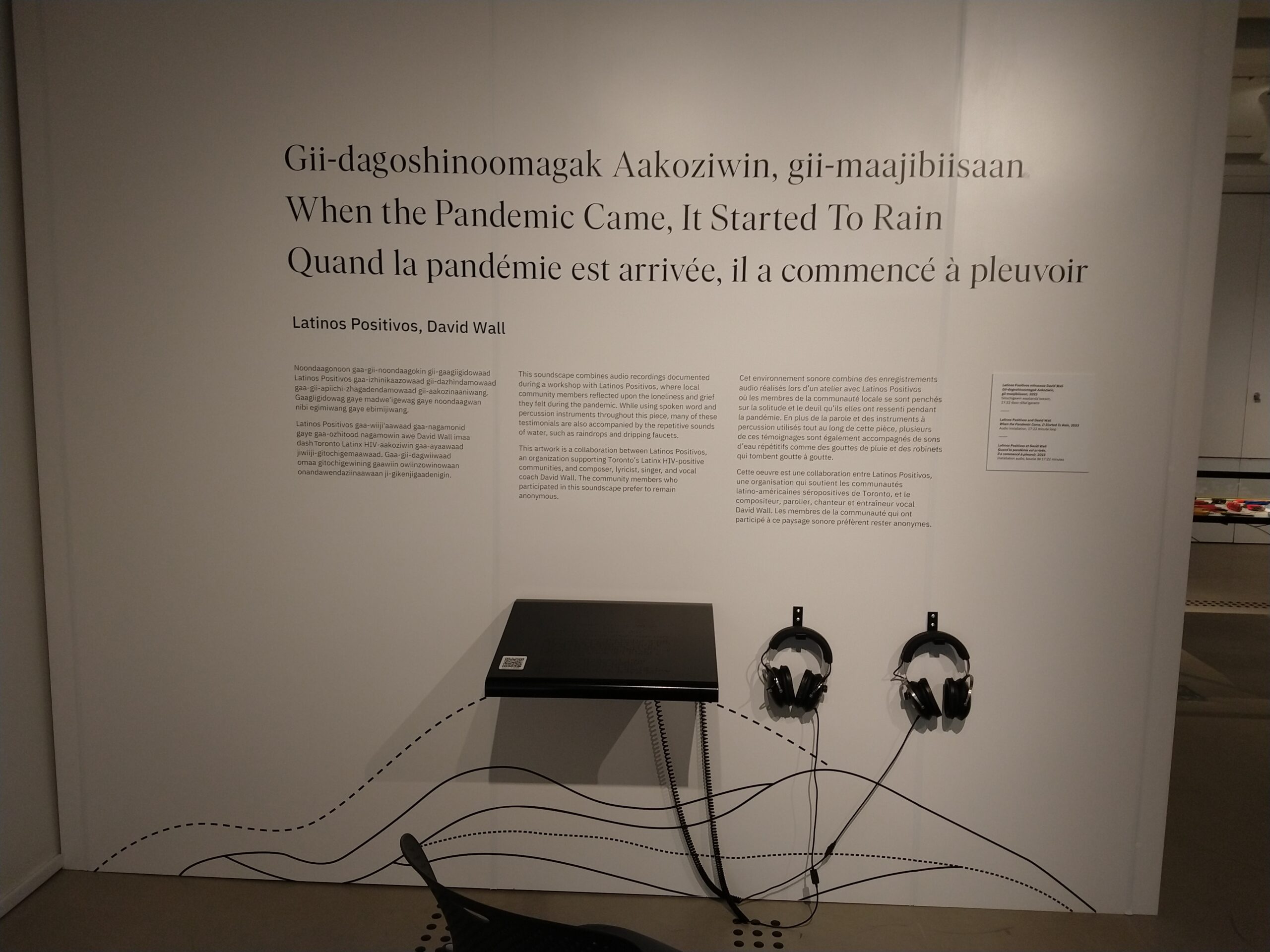 A white wall with black text. There are two sets of headphones hanging on the wall.
