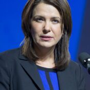 Photo of a white woman with shoulder-length brown hair wearing blue and black in front of a blue background.
