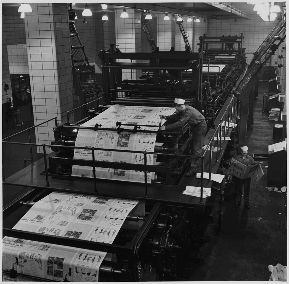 Black and white photo of a man working a huge industrial printing press.