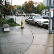Colour photo of a city street corner with a police car marked "Metro Police" in the midground. Labeled "City of Toronto Archives, Series 1465, File 169, Item 144."