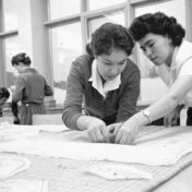 Black and white photo of two teenage girls bent over a table, working with fabric.