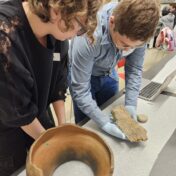 Group of young university students handle archeological materials in classroom setting.