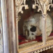 A colour photograph of a human skull with "Brebeuf" written across the forehead. The skill is ensconced in a highly decorated gold cabinet on a red cloth.