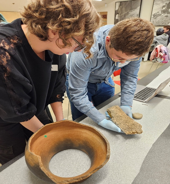 Group of young university students handle archeological materials in classroom setting. 