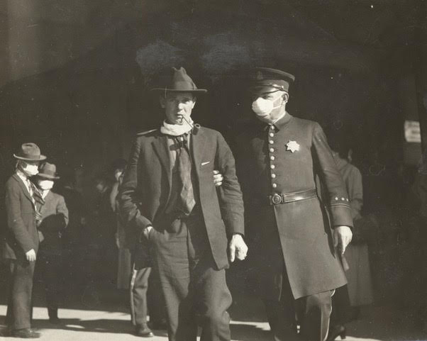 Black and white historic photograph. Depicts a police officer in pea coat wearing mask and apprehending a civilian who had lowered his mask. 