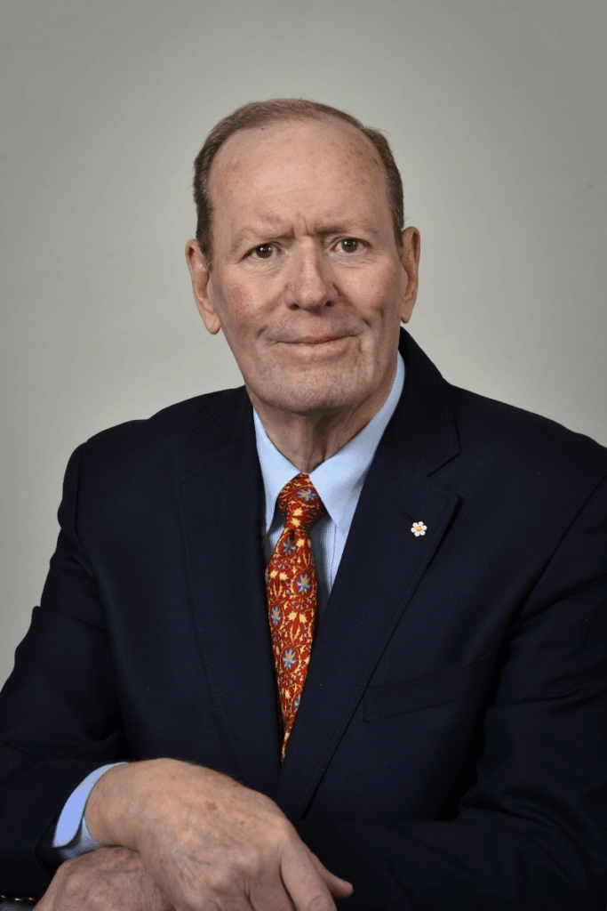 Portrait photograph of an older man wearing a suit, with brown eyes and a warm closed-mouth smile