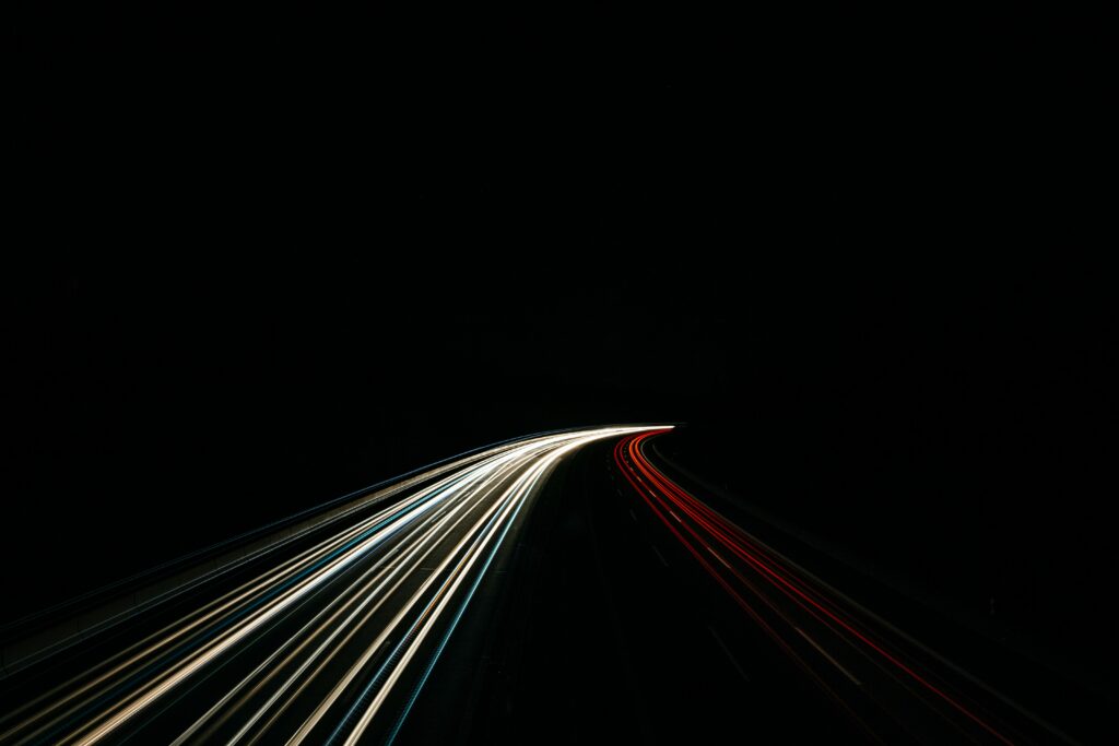 Long exposure photograph of light trails on a highway at night, with white and yellow streaks curving to the left and red streaks on the right against a black background