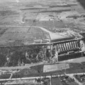 Aerial black-and-white photograph of the Queenston-Chippawa hydroelectric generating station, showing the large powerhouse building at the base of a cliff with penstocks (water conduits) visible along the slope, surrounded by rural farmland and roads, likely taken in the early 1920s during or shortly after construction.