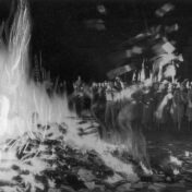 Black and white photo of a crowd of people, some in military uniforms, throwing books into a huge bonfire.