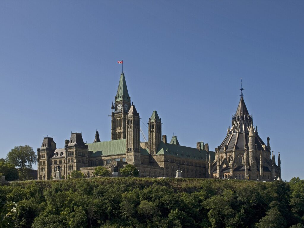 Colour photo of the Canadian Parliament's Centre Block and Library seen from a lower level and a distance.