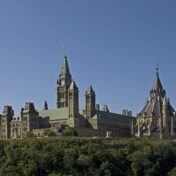 Colour photo of the Canadian Parliament's Centre Block and Library seen from a lower level and a distance.